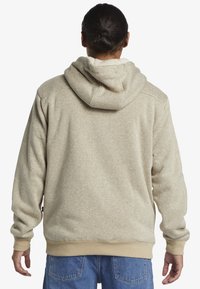 Felpa beige con cappuccio realizzata in tessuto texturizzato, dotata di una morbida fodera interna, polsini a costine e tasca a marsupio sul davanti.
