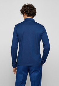 Marinblå långärmad polo skjorta med krage, gjord av ett mjukt tyg. Har en subtil textur och en figurnära design.