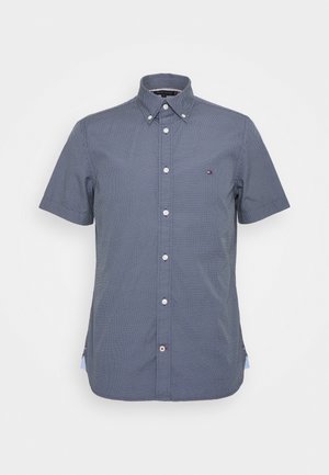 Granatowa koszula z krótkim rękawem, zapinana na guziki, z delikatnym białym geometrycznym wzorem, kołnierzykiem na guziki oraz małym logo na lewej piersi.