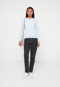 Gaiši zils garām piedurknēm tops, melnas džinses, baltas apavas, turēt mazu bēša krāsas pleca somu. Vienkārša dizaina ar ikdienišķu piegriezumu.