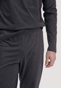 Dunkelgraues Loungewear-Set mit langärmligem Oberteil und elastischem Bund an der Hose. Weiche, glatte Textur mit lässigem Schnitt und minimalen Details.