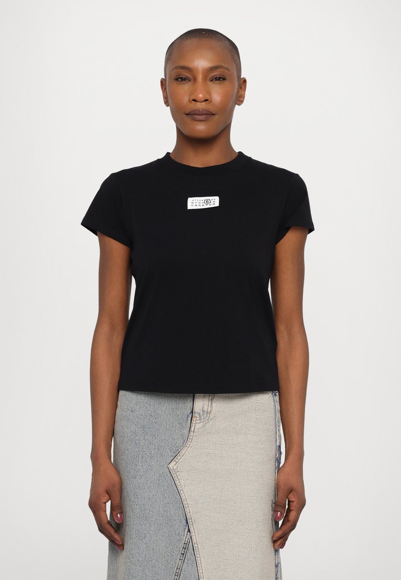 Black short-sleeve t-shirt with a rounded neckline and a white rectangular tag on the front featuring printed text. Smooth, lightweight fabric.
