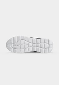 Semelle d'une chaussure de sport noire et blanche montrant une semelle extérieure en caoutchouc blanc texturée et détaillée avec des rainures courbées et rectangulaires pour l’adhérence.