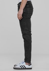 Jeans de mezclilla negros con un corte ajustado, diseño de cinco bolsillos y detalles de costura sutiles, combinados con zapatillas blancas y negras.