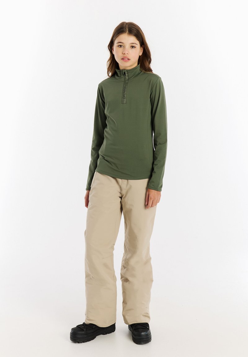 Donkergroene trui met lange mouwen en een ritskraag; gecombineerd met lichtbeige, losse broek en zwarte, gestructureerde schoenen.