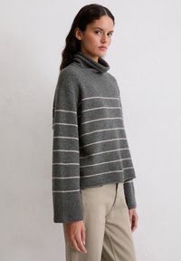 Ciemnoszary sweter z wysokim kołnierzem, z kremowymi poziomymi paskami, szerokimi rękawami i luźnym krojem. Miękka tekstura.