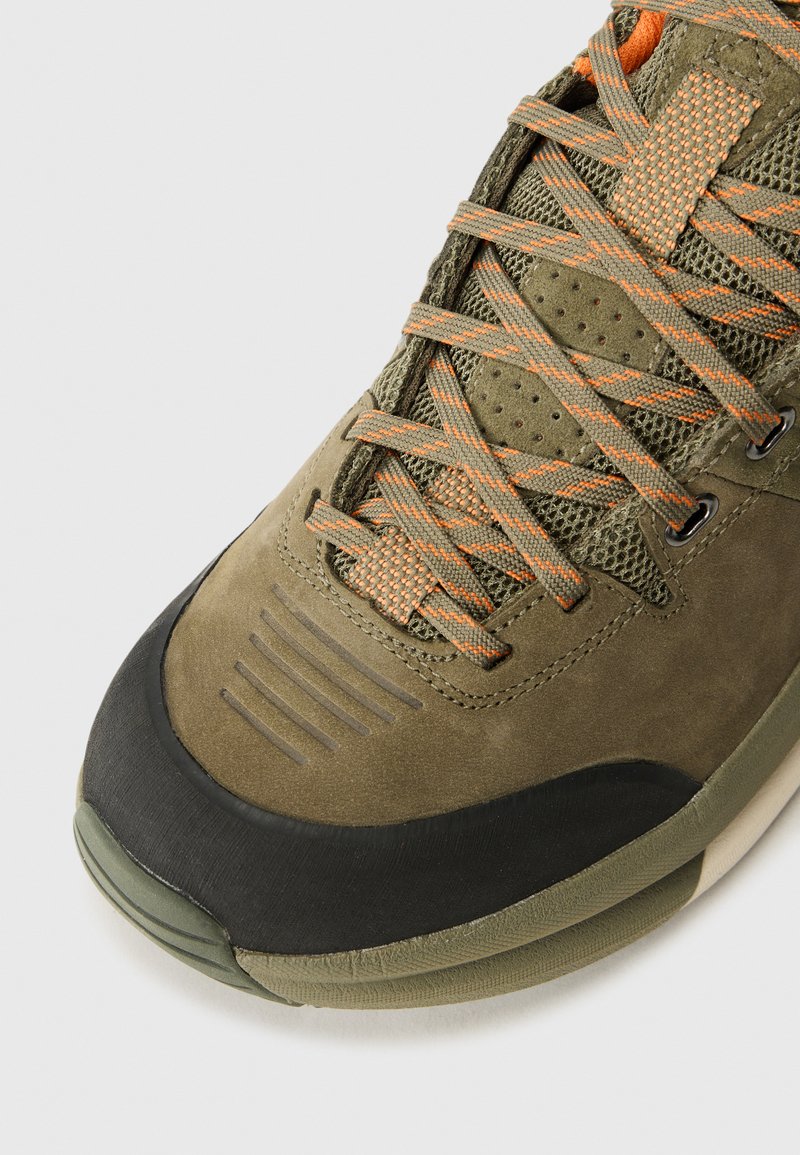 Oliwkowe sneakersy z pomarańczowymi akcentami, z siateczkowym i zamszowym wykończeniem, grubą czarną gumową osłoną palców oraz szczegółowym systemem sznurowania.