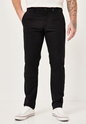 Black cotton chinos with a straight fit, flat front, and side pockets. Paired with white low-top sneakers featuring red accents.