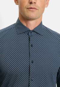 Navy-blaues Hemd mit geometrischem Muster. Der Stoff hat eine glatte Textur und ist mit einem Punktkragen sowie dunkelbraunen Knöpfen versehen.