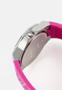 Oktagonalt silverfodral med ett rosa gummiband som har ett geometriskt mönster; inkluderar en krona för justering och en slät, polerad baksida.