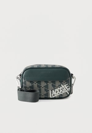 Sac bandoulière Lacoste vert foncé avec motif géométrique, bandoulière amovible et logo Lacoste blanc sur la poche avant.