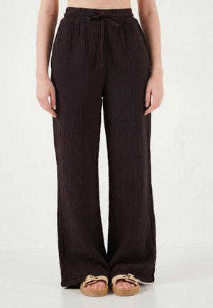 Parte inferiore del corpo femminile indossando pantaloni neri larghi e arricciati con cintura elastica e sandali beige con fibbie dorate.