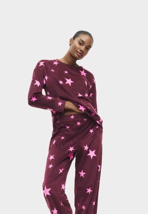 Bordeaux loungewear set met roze sterpatronen op een zachte stof. De top heeft lange mouwen; de broek heeft een ontspannen pasvorm met een elastische tailleband.