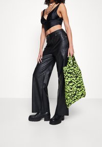 Černý saténový crop top, černé kalhoty z umělé kůže s vysokým pasem, robustní černé platformové boty a taška s neonově zeleným vzorem.