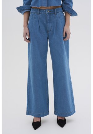 Lichtblauwe wijde denim broek met plooien, hoge taille en een rafelige zoom. Gecombineerd met zwarte pumps met spitse neuzen.