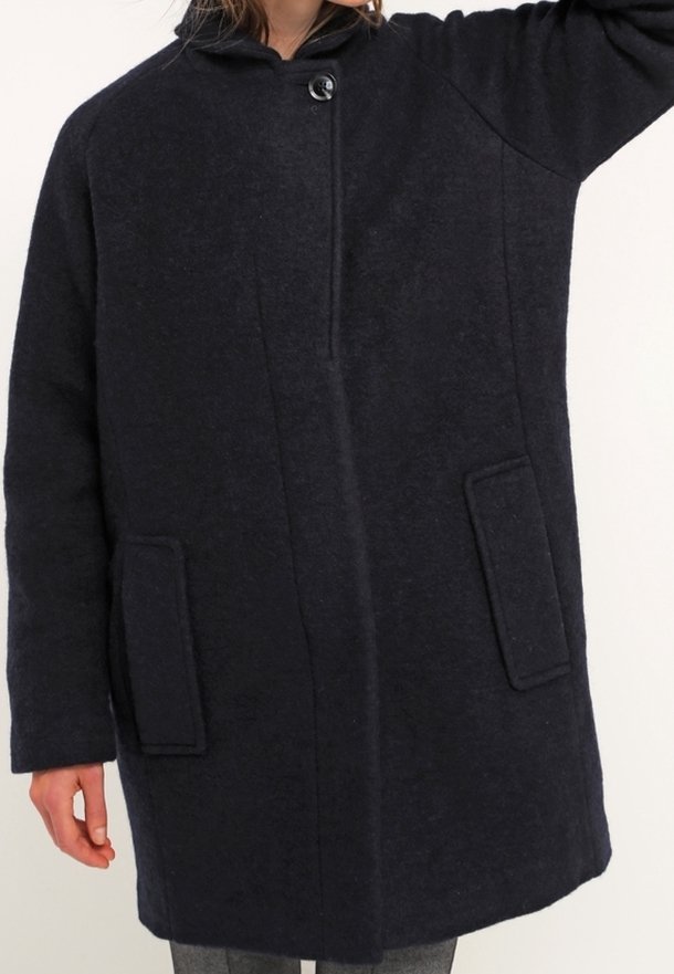 Manteau en laine bleu marine avec col montant, fermeture à boutons sur le devant et deux grandes poches plaquées. Présente une coupe ample et un tissu texturé.