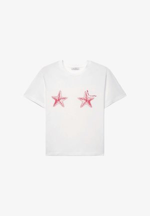 Maglietta bianca a maniche corte con due stelle marine rosse stampate sull'area del petto e un piccolo testo rosso vicino alla stella marina destra.