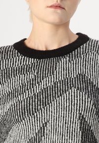 Svart och off-white stickad tröja med ett texturerat zick-zack-mönster, rund svart halsringning och ribbat detaljer genom hela plagget.