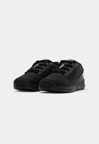 Zapatos deportivos negros con una parte superior texturizada, cordones negros y acentos verdes. Presenta una suela acolchada y un diseño de puntera redondeada.
