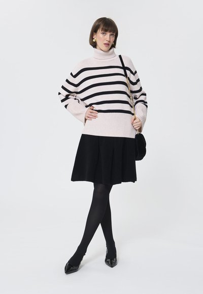 Wzorzysty sweter z golfem w jasnoróżowym i czarnym kolorze, zestawiony z czarną rozkloszowaną spódnicą. Modelka nosi czarne rajstopy i czubate szpilki.