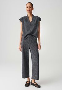 Grauer strukturiertes Strickoberteil mit kurzen Ärmeln und V-Ausschnitt, kombiniert mit passenden weit geschnittenen Hosen. Schwarze perforierte Schuhe runden das Outfit ab.