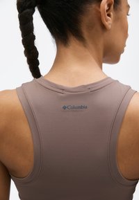 Gros plan sur une personne aux cheveux tressés portant un haut marron sans manches de la marque Columbia, vue de dos.