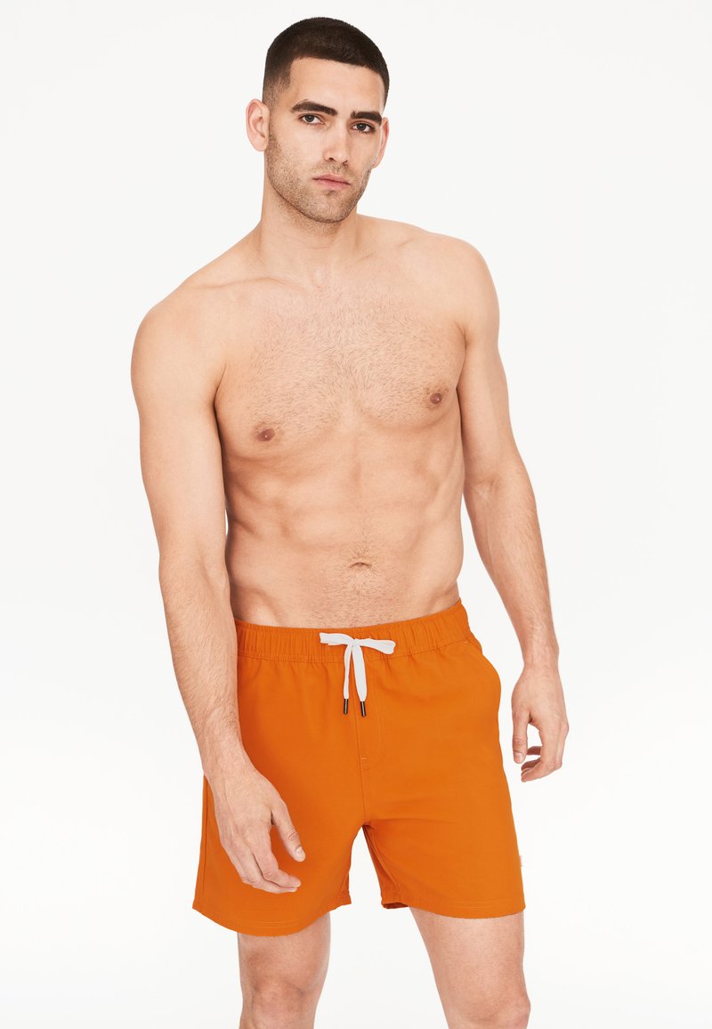 Oranžové plavecké šortky s elastickým pasem a bílým šnůrkovým stahováním. Hladká látka s délkou do poloviny stehna a bez viditelných vzorů či akcentů.