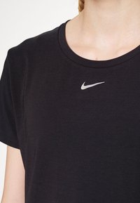 Närbild av en person som bär en svart Nike-t-shirt med en liten vit Nike-swoosh-logotyp under halsringningen.