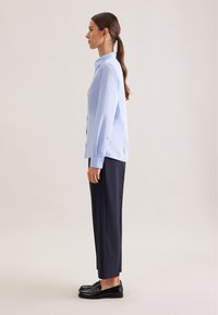 Lichtblauw overhemd met knopen en lange mouwen, gecombineerd met donkerblauwe broek en zwarte loafers. Gladde stof en een getailleerde pasvorm.