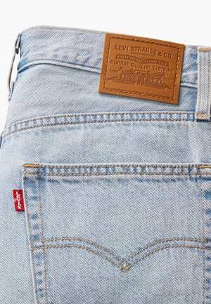 Zadní kapsa světlých modrých džín s oranžovým prošitím, červená štítek Levi's a hnědá kožená značka Levi Strauss & Co. na pásu.
