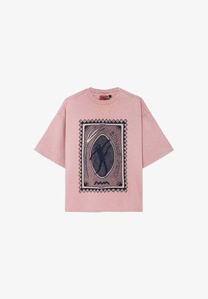 Różowy, oversize'owy T-shirt z nadrukiem graficznym, przedstawiającym ciemnoniebieski wzór i napis "HOLIDAY PORTAL" oprawiony w geometryczny wzór.