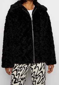 Svart imitationspälsjacka med dragkedja fram, bred krage och långa ärmar. Har en mjuk textur med en fluffig utseende.