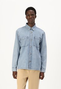 Ανοιχτό μπλε τζιν πουκάμισο με μακριά μανίκια, κουμπιά μπροστά, δύο τσέπες στο στήθος και γιακά σε σχήμα πέτου. Λείος υφασμάτινος χαρακτήρας με κλασικό σχέδιο.