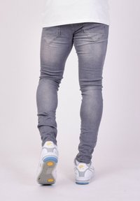 Jeans grigi slim-fit con una texture sbiadita, abbinati a sneakers bianche con dettagli gialli e blu. La vista posteriore mostra i dettagli delle tasche.