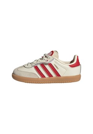 Baskets Adidas Samba blanches et rouges avec semelle en gomme, laçage à l'avant et trois bandes rouges sur le côté.