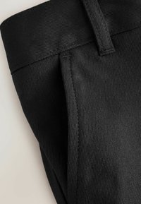 Schwarze Baumwollhosen mit flachem Bund, sichtbaren Nähten und glatter Textur. Sie verfügen über ein tailliertes Design und keine sichtbaren Beschläge.