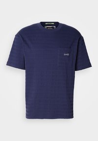 T-shirt bleu marine à manches courtes avec un tissu texturé, présentant des rayures horizontales et une petite poche poitrine avec un logo.