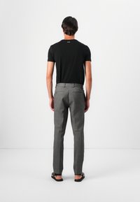 Svart åtsittande t-shirt, grå skräddarsydda byxor med ett subtilt mönster, platta sandaler, sett bakifrån mot en neutral bakgrund.