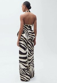 Schwarzes und weißes Zebra-Design Haltertop mit schwingendem Peplum, kombiniert mit weiten Hosen, die goldene Akzente und strukturierten Stoff aufweisen.