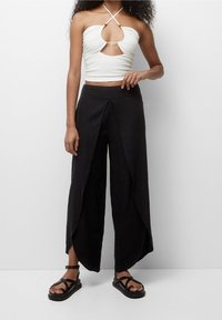 Haut blanc court avec un design découpé et un tissu texturé ; associé à un pantalon large noir ample avec un style drapé unique.