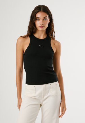 Schwarzes, geripptes Tanktop mit hohem Hals und Racerback-Design, mit kleinem weißen Logo auf der Brust. Kombiniert mit hellen Hosen.