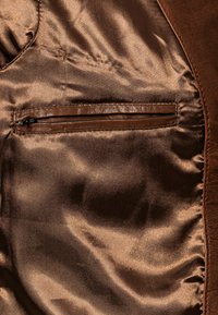 Braune Satininnenseite einer Jacke mit einem sichtbaren Reißverschlussfach. Der Stoff hat eine glatte, glänzende Textur und wird von einem braunen Wildlederaußenstoff ergänzt.