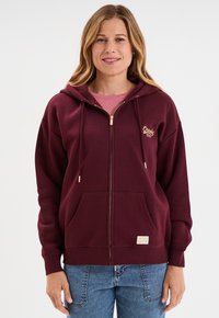 Felpa borgogna con zip, tasca a marsupio, zip color oro, cordini e una piccola etichetta sulla parte anteriore, realizzata in tessuto morbido.