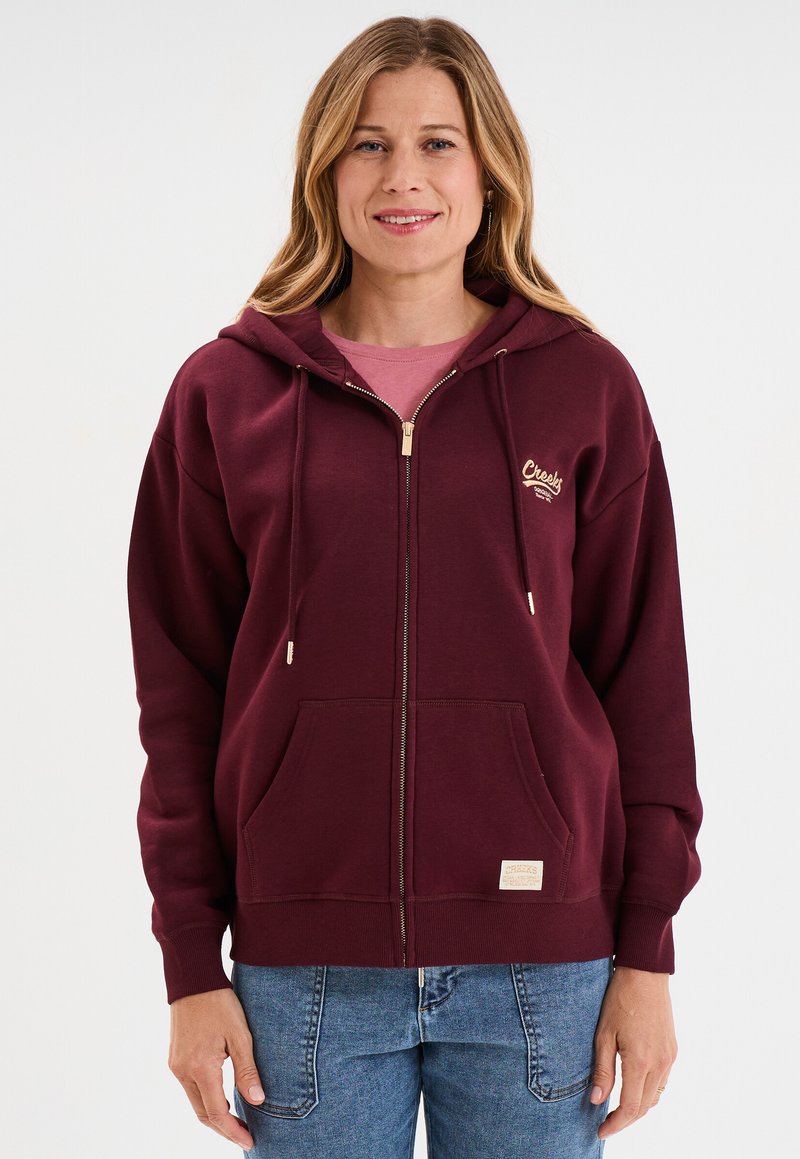 Felpa borgogna con zip, tasca a marsupio, zip color oro, cordini e una piccola etichetta sulla parte anteriore, realizzata in tessuto morbido.