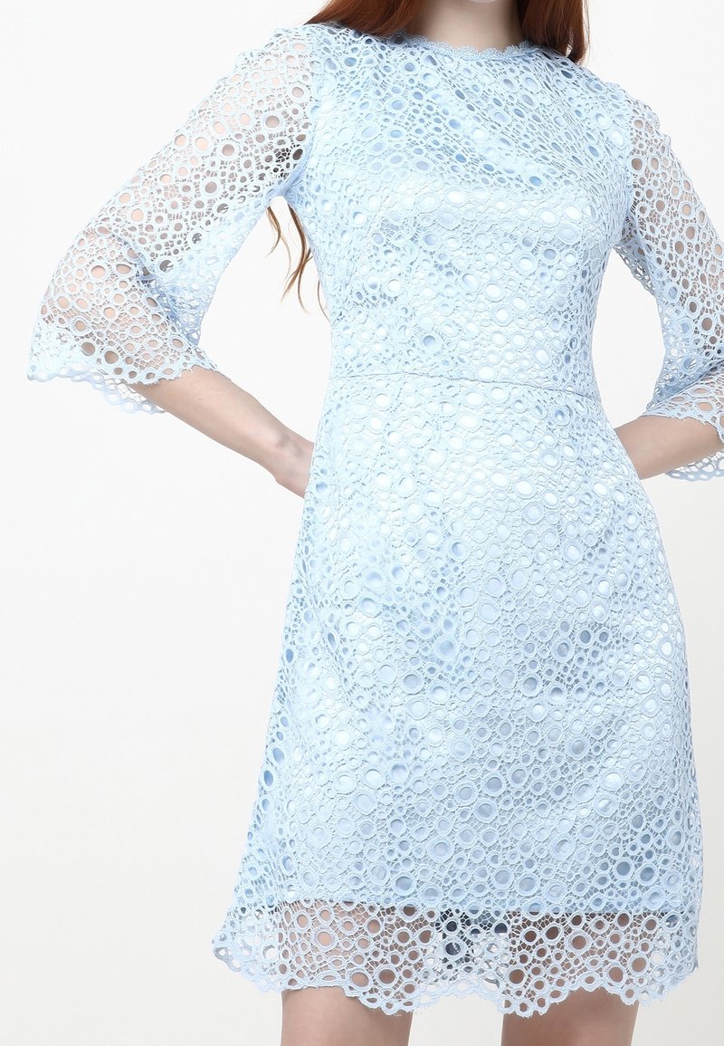 Ljusblå spetsklänning med cirkelmönster, trekvartsärmar, scallopad nederkant och figursydd midja. Texturen är genomskinlig och lager-på-lager.