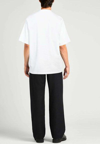 T-shirt bianco a maniche corte con una vestibilità rilassata, abbinato a pantaloni scuri larghi. Il tessuto appare liscio, senza motivi o loghi visibili.