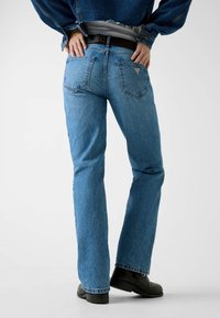 Jean en denim bleu évasé avec une coupe classique, doté d'une taille mi-haute, de deux poches arrière et de légères usures au niveau de l'ourlet.