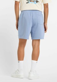 Light blue athletic shorts with an elastic waistband, a single back pocket, and a smooth fabric texture. Worn with white shoes and socks.