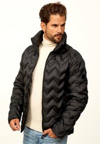 Black puffer jacket with a chevron pattern, zipper closure, and high collar. Features smooth, shiny material and a side pocket.
