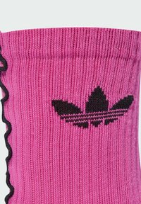 Calzino rosa lavorato a maglia con texture a coste, bordo ondulato nero, con il logo Adidas nero sul lato caratterizzato da tre forme simili a foglie.